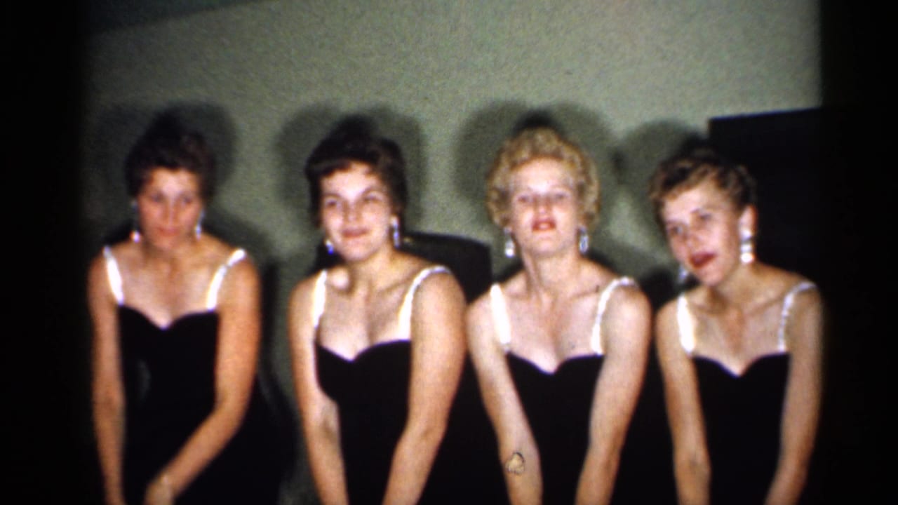The four women face the camera in matching dark dresses, with one leaning in and the group settling into a posed moment in 1958 New Jersey footage.