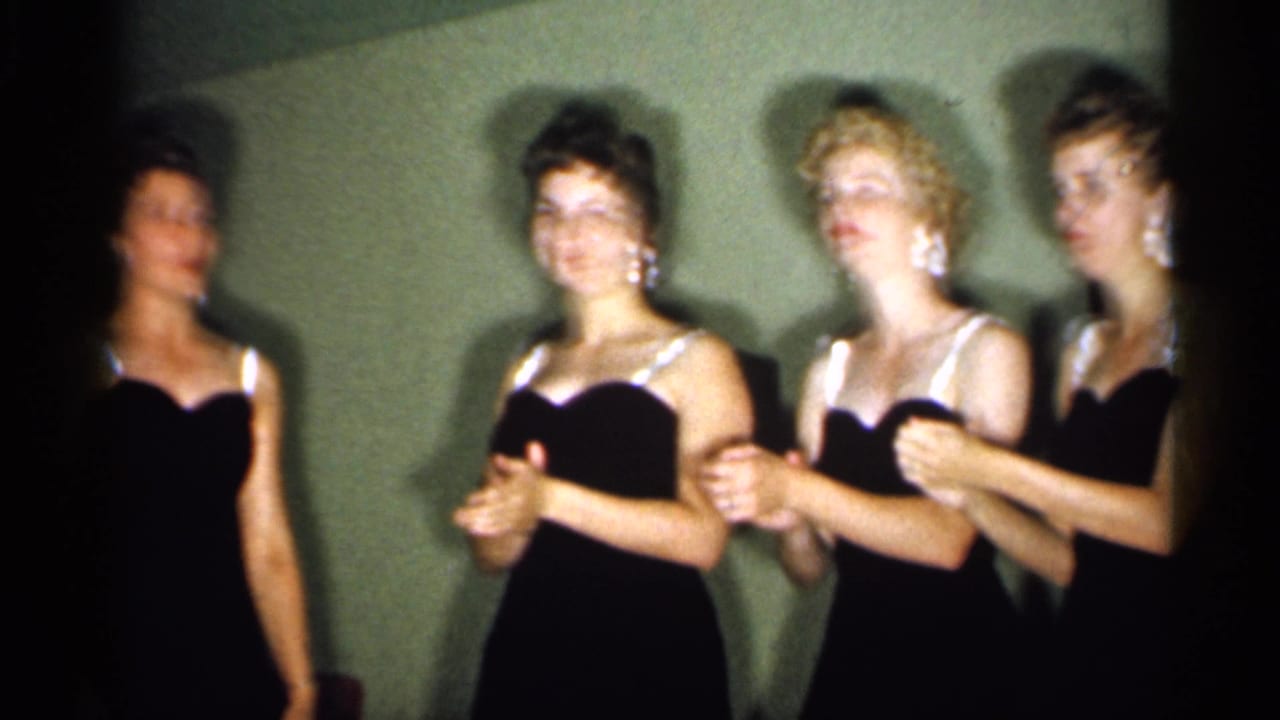 Four young women in black evening dresses with white strap details stand in formation indoors in 1958 New Jersey footage.