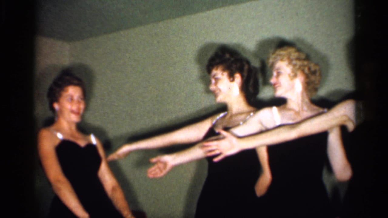 The group continues a synchronized arm movement indoors, with black evening dresses and wall shadows visible in the 1958 New Jersey footage.