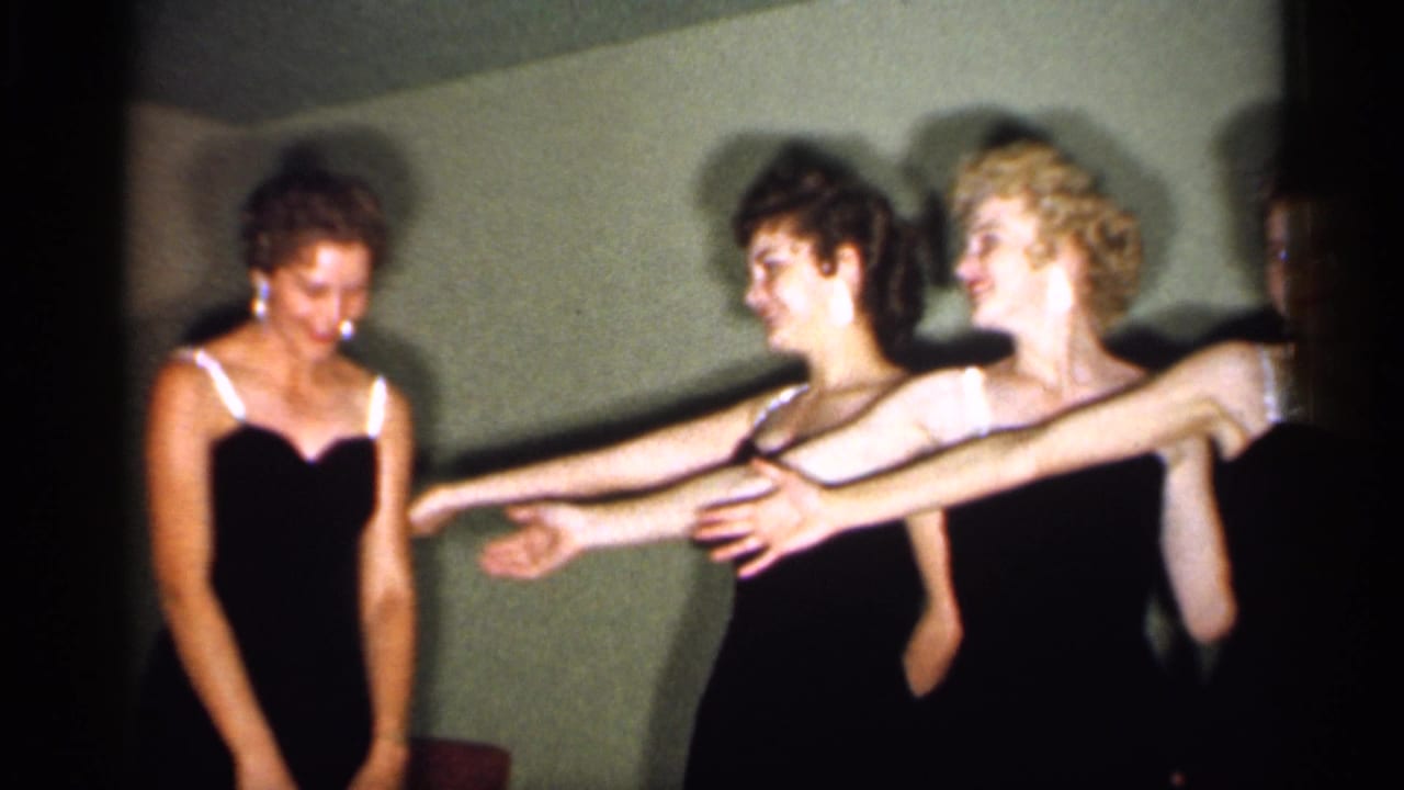 Four women in black dresses begin a coordinated dance pose indoors.