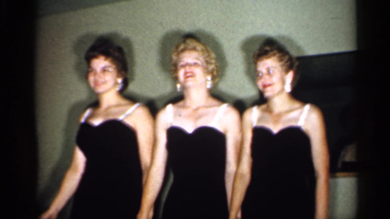 Three adult women in black dresses with white trim stand in a row during the 1958 New Jersey indoor dance footage.