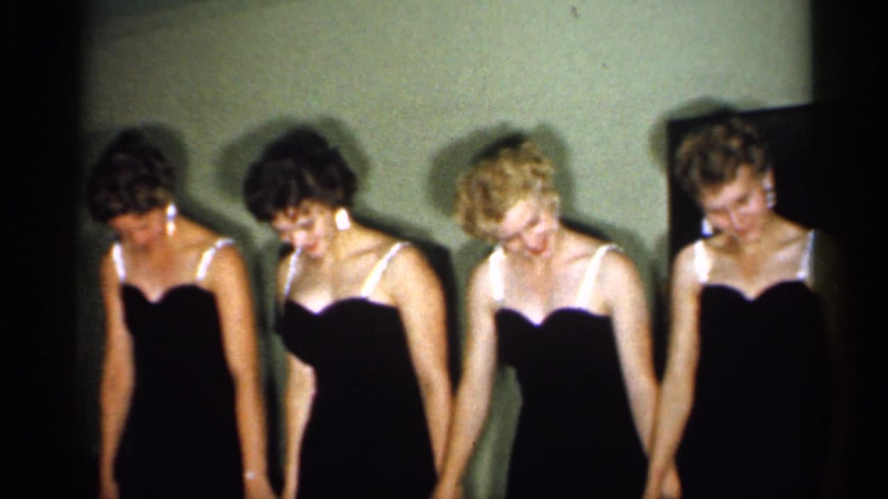 Four adult women in coordinated black dresses bow together in a 1958 New Jersey home-movie interior.