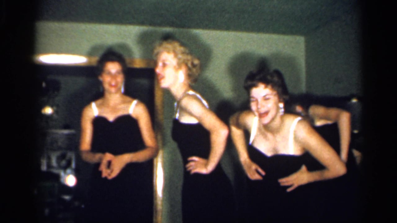 Young women in black dresses with white straps pose playfully toward the camera in archival 1958 New Jersey home-movie footage.