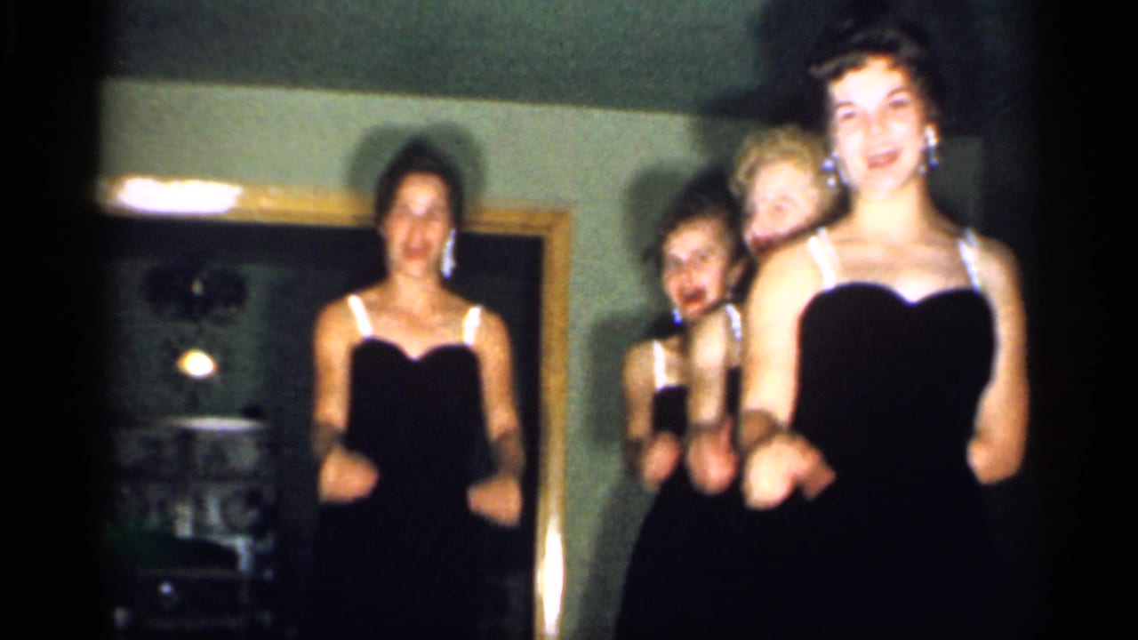 The group moves in unison toward the camera, smiling in a private New Jersey interior captured on 8mm film in 1958.