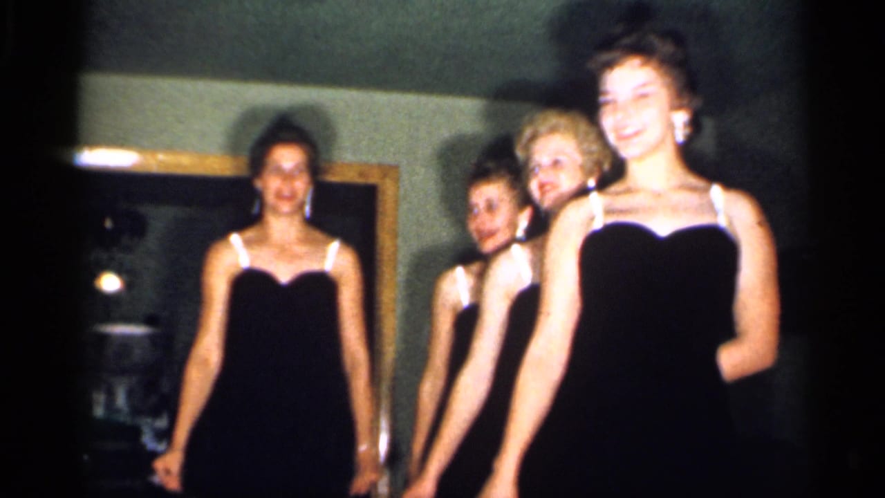 A woman in front smiles as three others line up behind her during the indoor 1958 New Jersey home-movie performance.