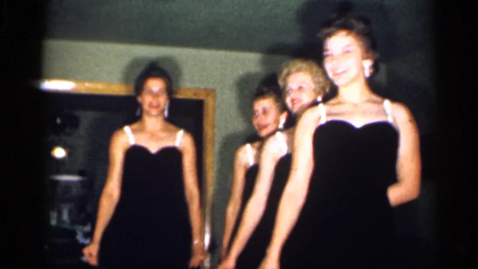 A woman in front smiles as three others line up behind her during the indoor 1958 New Jersey home-movie performance.