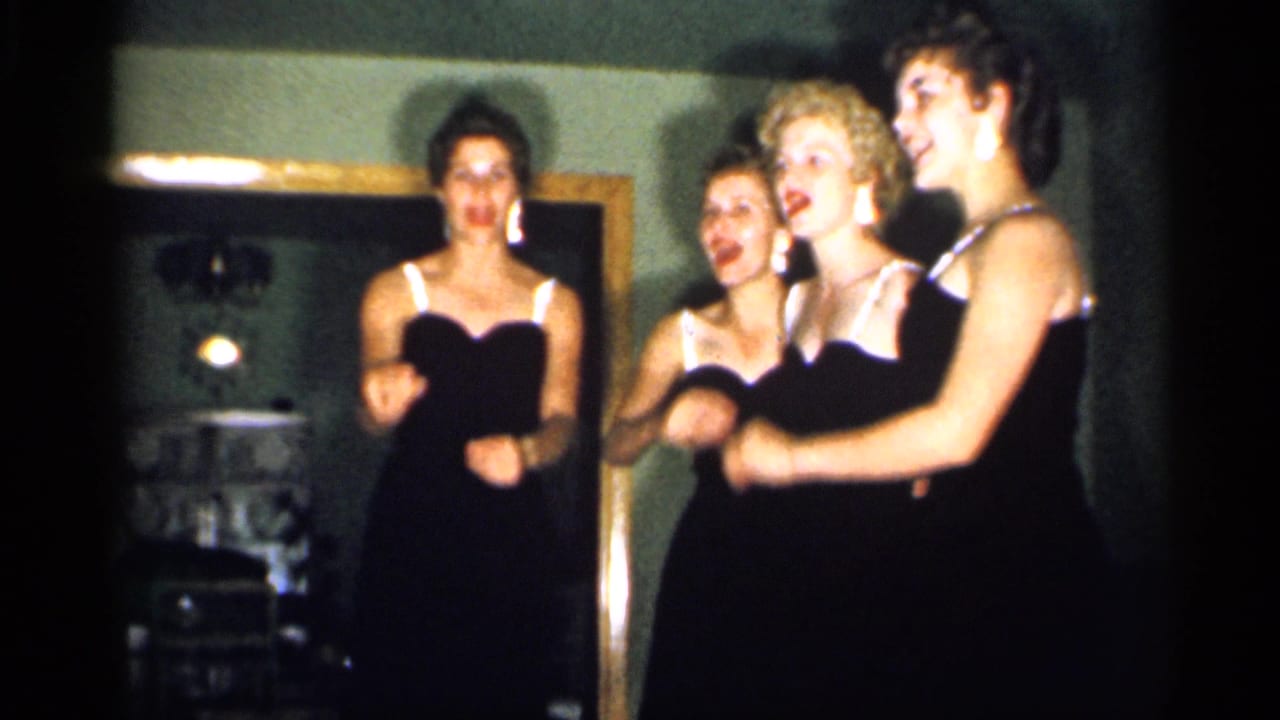 The group faces the camera in matching dark dresses, smiling and gesturing during a 1958 New Jersey home performance.