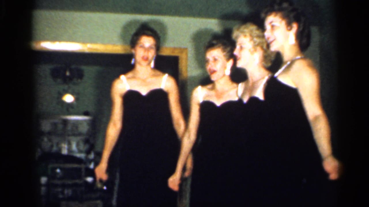 Four young women stand side by side in black evening dresses, framed by a doorway and dim room lighting in 1958 New Jersey footage.