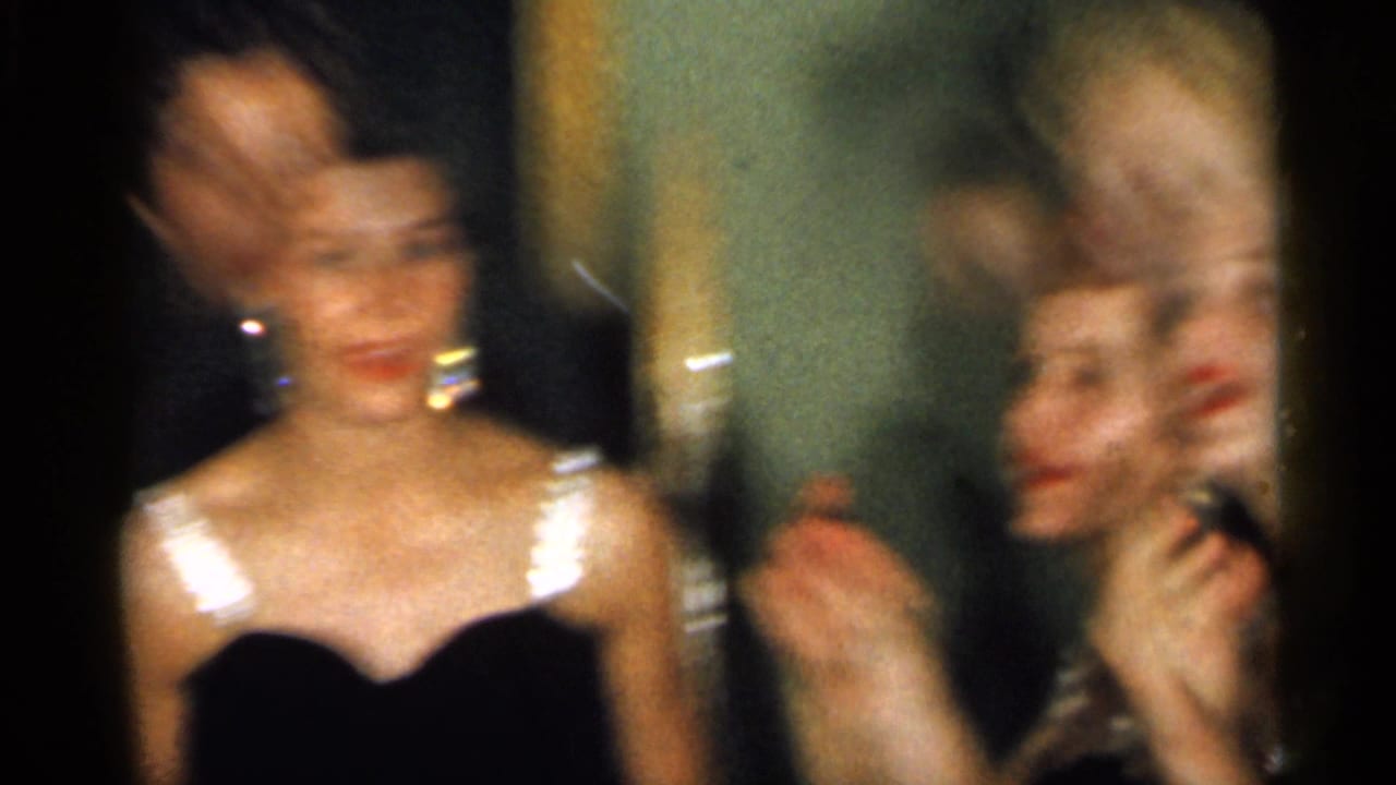 Two women in black formal dresses appear in a soft, blurred 1958 New Jersey home-movie frame as one claps.