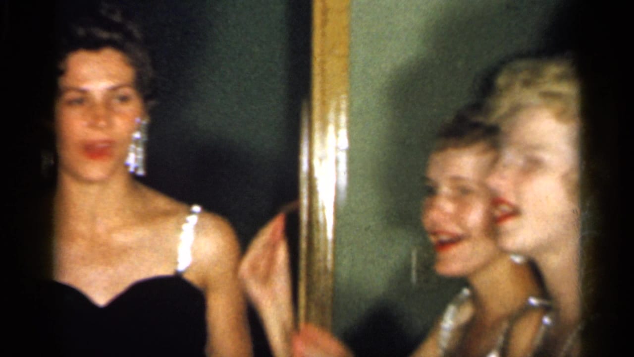 Two young women in black dresses pose near a mirror, with another face partly visible.