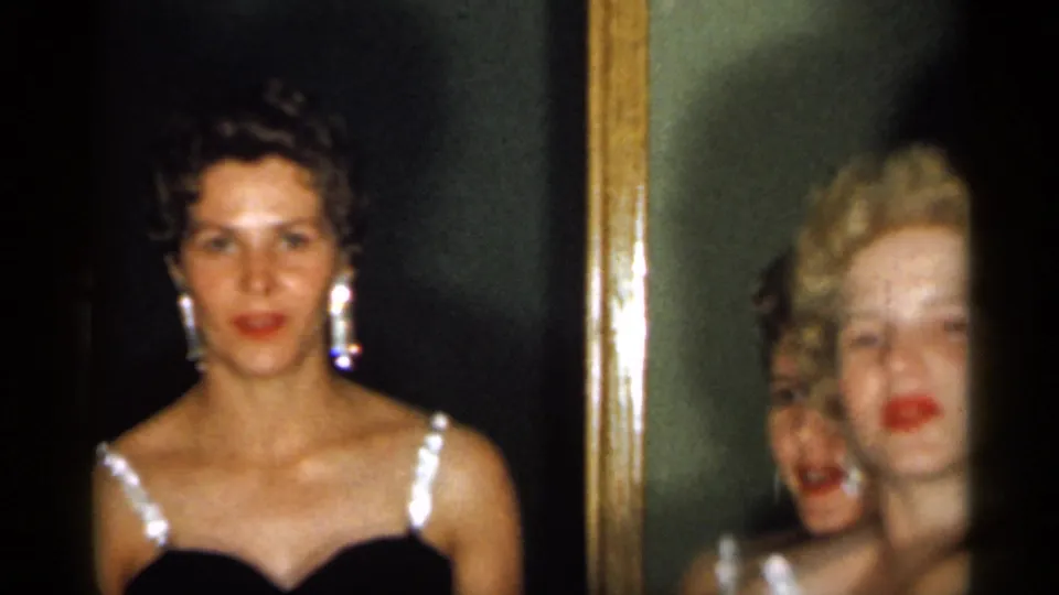 Young women in coordinated black dresses appear beside a mirror, with one woman facing forward and others partly visible behind her.