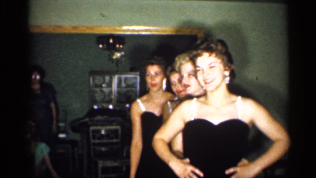 In a 1958 New Jersey home interior, four young women in matching dark dresses pose closely while one smiles with hands at her waist.