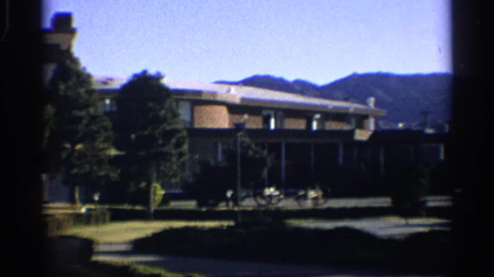 A low motel building sits below the mountains, with a bicycle near the front and trees along the grounds.