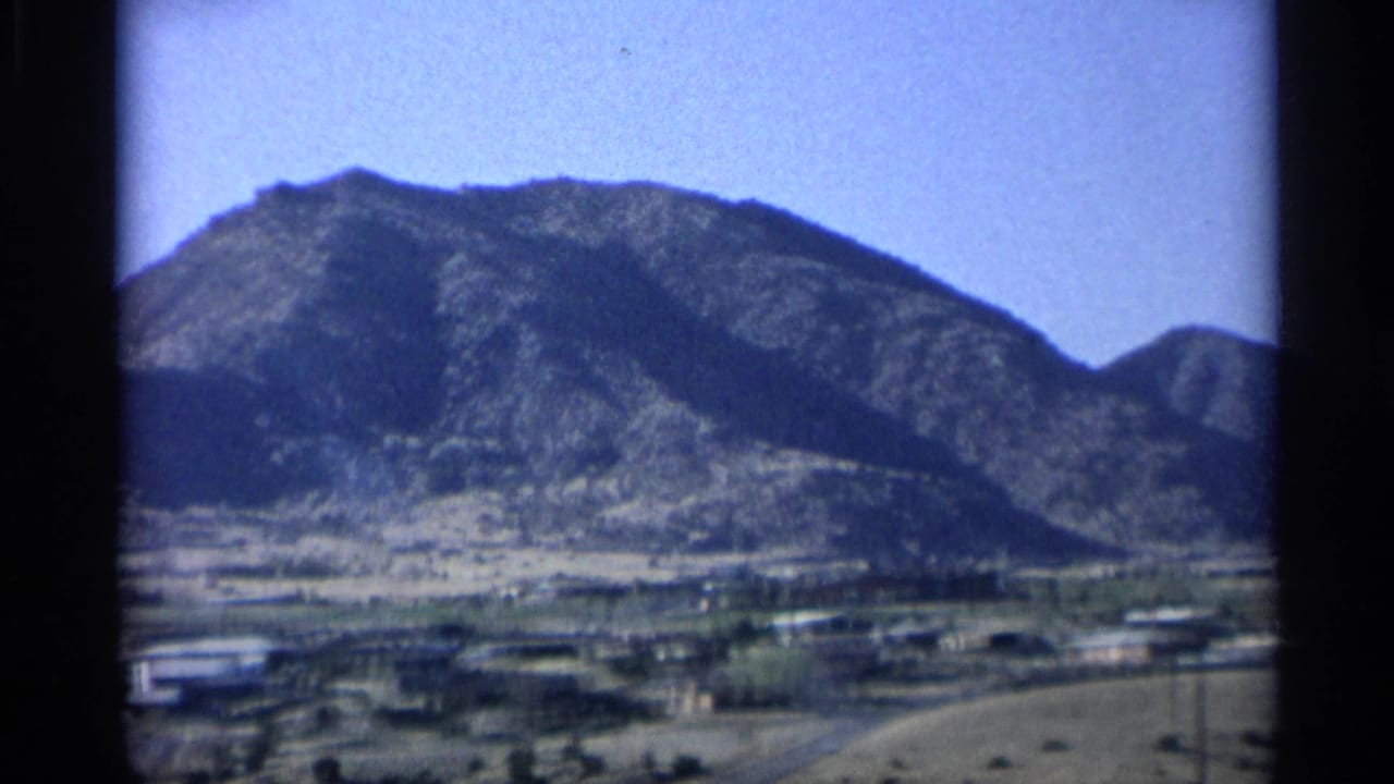 Desert town at the base of rugged mountains under a blue sky.