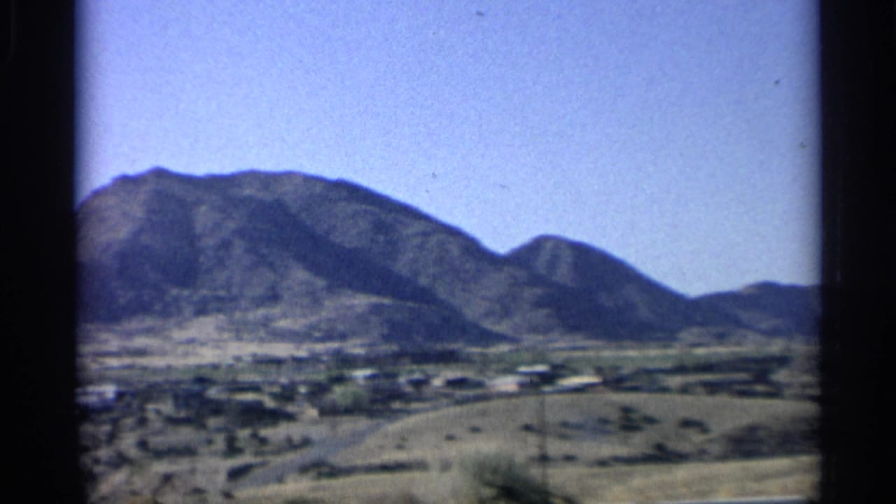 Mountain range and scattered desert buildings viewed across open land.