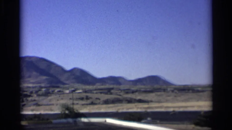 1959 Arizona 8mm view across arid land toward low mountains, with a road edge or wall visible at the bottom.