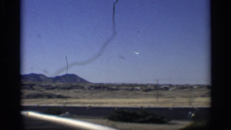 1959 Arizona frame showing a broad desert panorama, distant hills, utility poles, and visible film scratches in the sky.