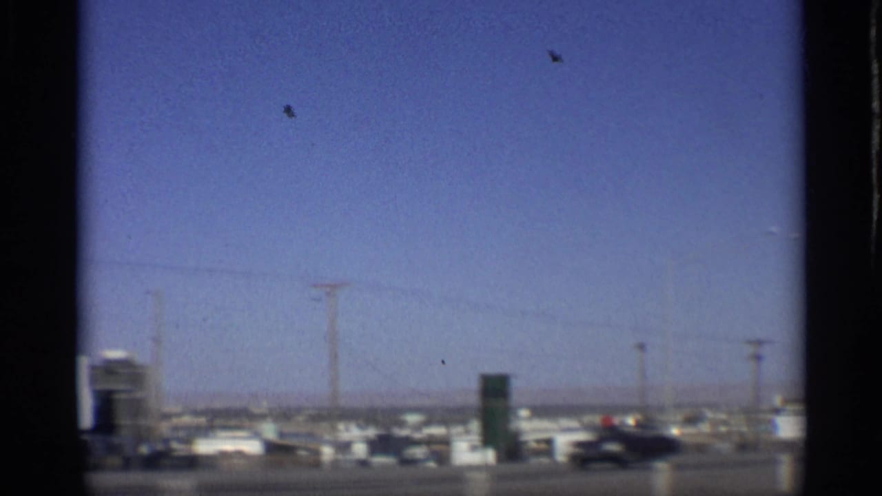 Roadside commercial area with billboards, utility poles and cars seen through a moving vehicle window.