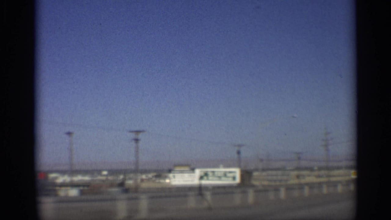 Highway roadside with a large billboard, low buildings and utility poles beyond the road.