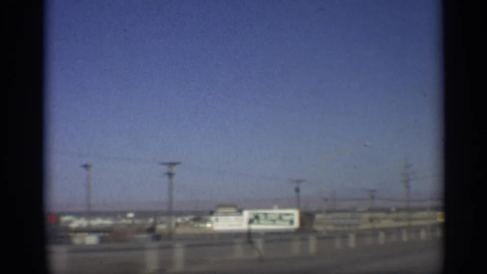 1959 Arizona roadside view with a large commercial billboard, low buildings, utility poles and open sky filmed from a moving car.