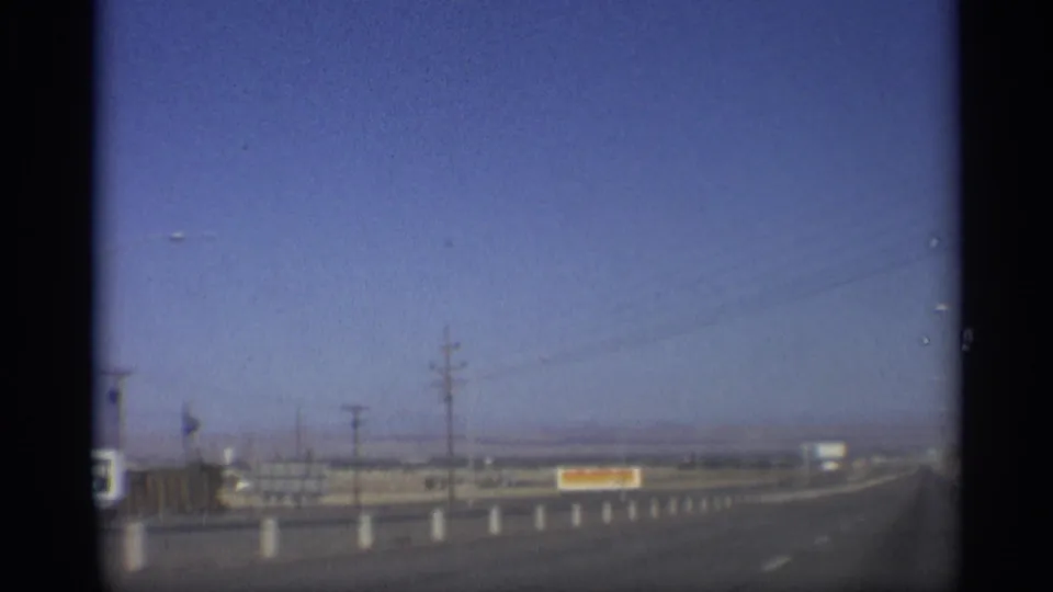 Arizona highway scene from 1959 showing a straight road, roadside sign, utility poles and distant low horizon from a moving vehicle.