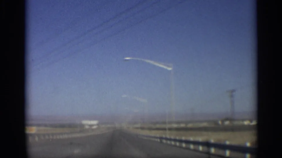 1959 Arizona highway view with guardrail, streetlight, power lines and sparse roadside buildings receding into the distance.