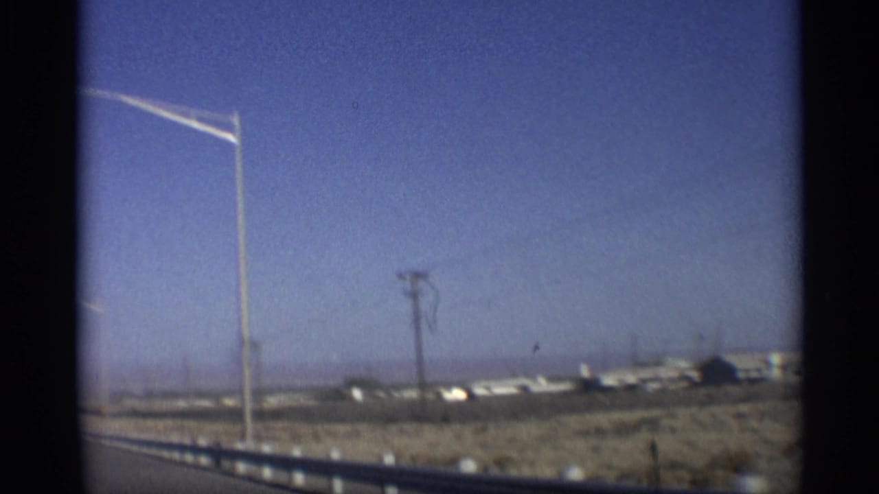 Roadside view with streetlight, utility pole, low buildings, desert ground, and distant horizon.