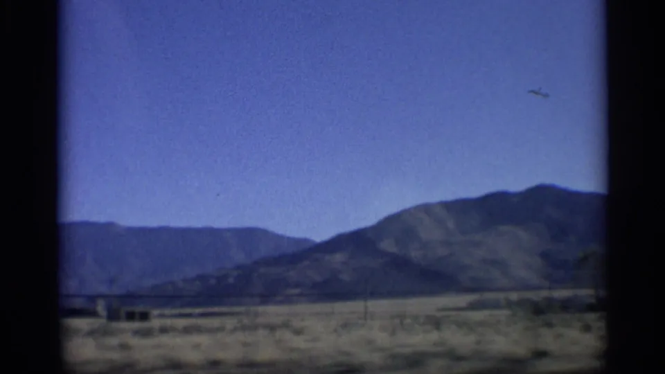 1959 Arizona vehicle-shot view of desert mountains, roadside poles, low structures, and a broad blue sky.