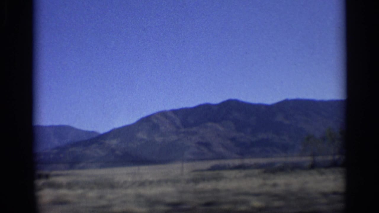 1959 Arizona home-movie frame showing a mountain range across a dry desert plain under a bright blue sky.