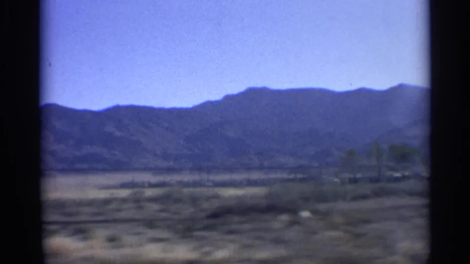 Moving-vehicle 8mm view of Arizona mountains and dry open land, with visible blur and film grain.