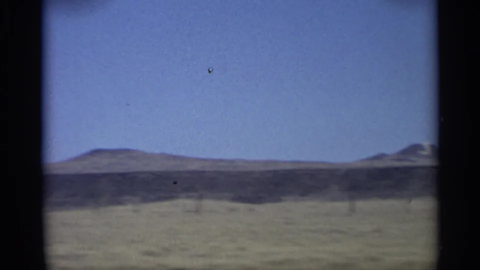 Arizona home-movie frame showing a broad arid plain, low distant hills, and an expansive blue sky.
