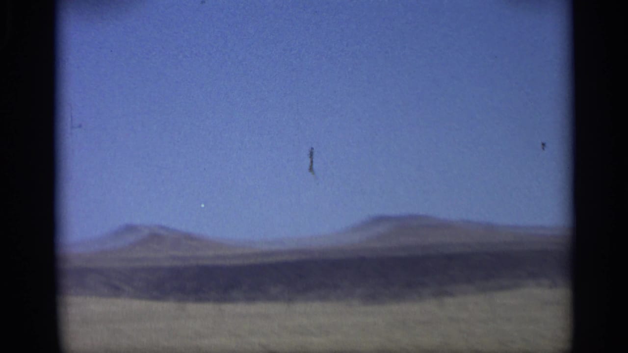 1959 Arizona home-movie view from a moving car across open land toward distant low hills and a clear blue sky.
