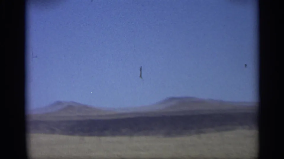 1959 Arizona home-movie view from a moving car across open land toward distant low hills and a clear blue sky.