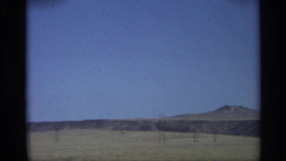 1959 Arizona roadside view across open terrain toward a small mountain and low ridge, filmed from a moving car.
