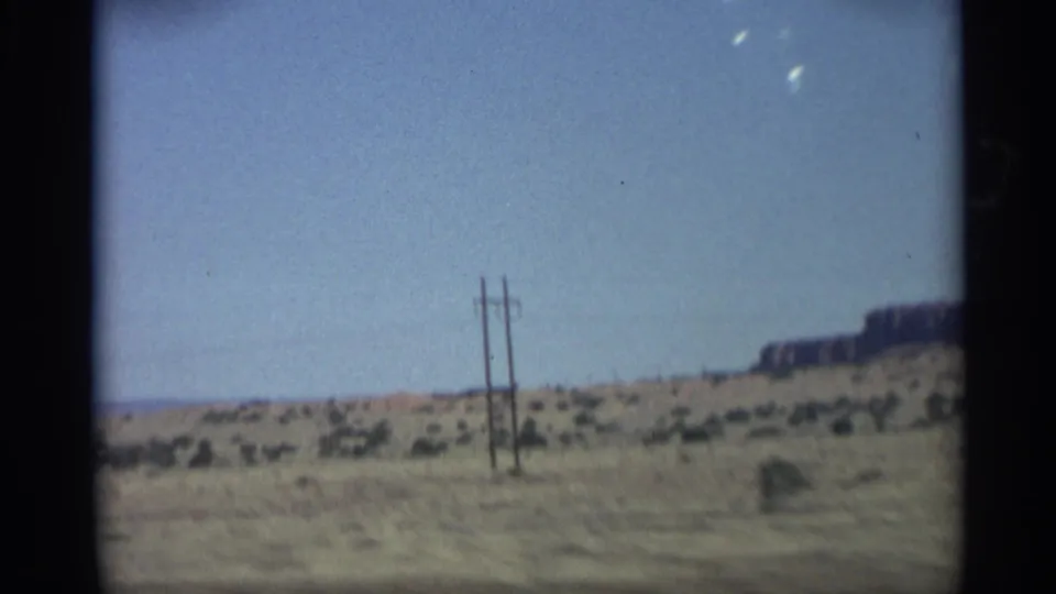 1959 Arizona moving-car view with utility poles, sparse shrubs, and distant cliffs across open desert land.