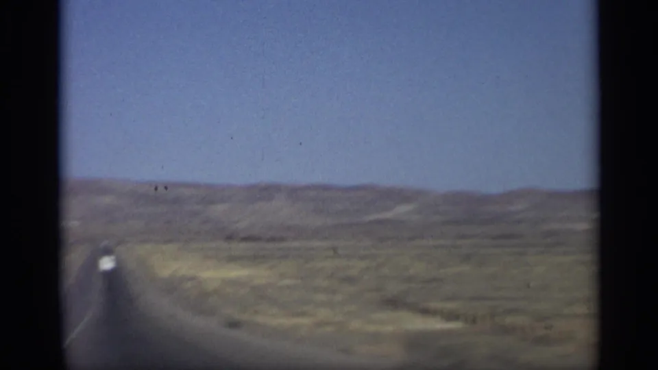 1959 Arizona road scene with a straight desert highway, low hills, and a distant white car ahead.