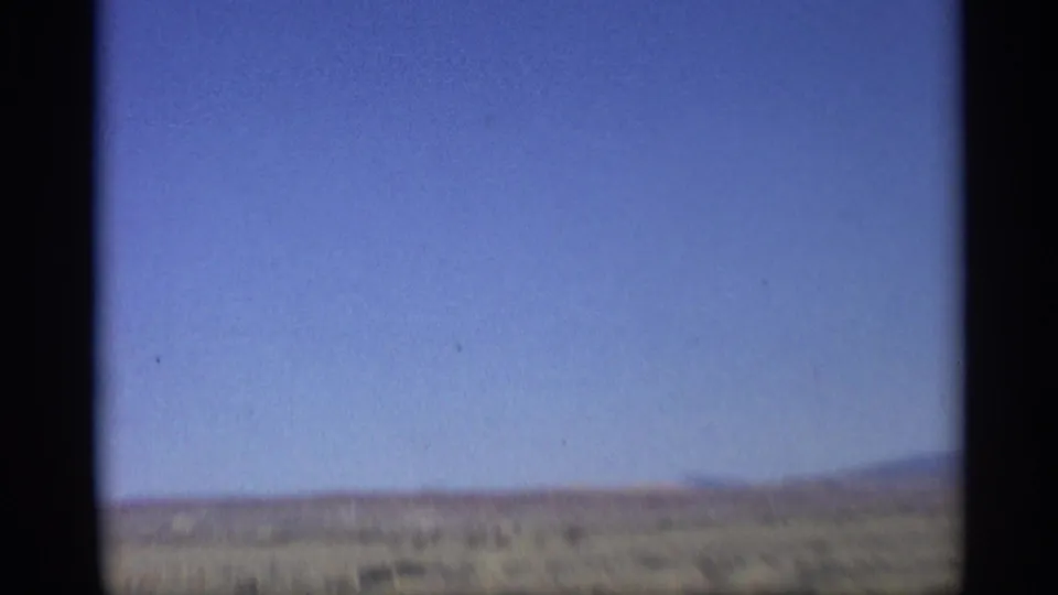 Soft 8mm frame of Arizona desert roadside, low brush, and blue sky recorded from a moving car in 1959.