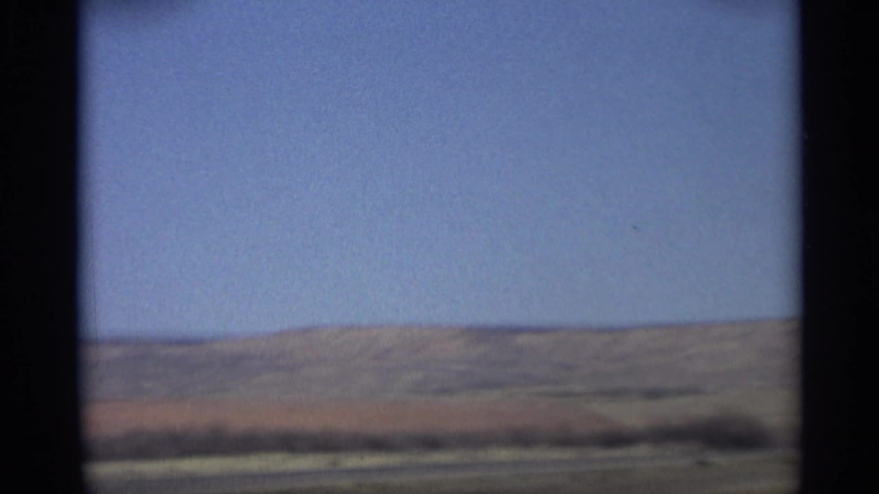 Open desert hills and blue sky seen from a moving vehicle.