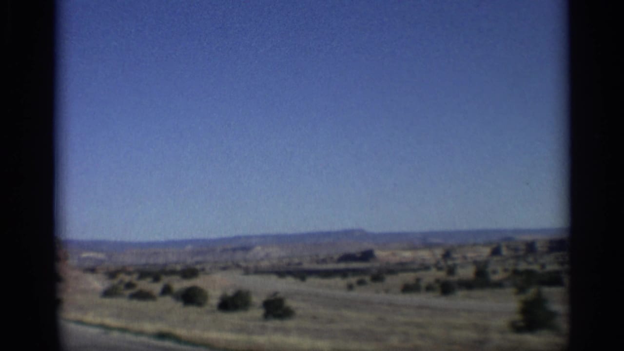 Open desert plain with scrub and low hills beneath a blue sky.