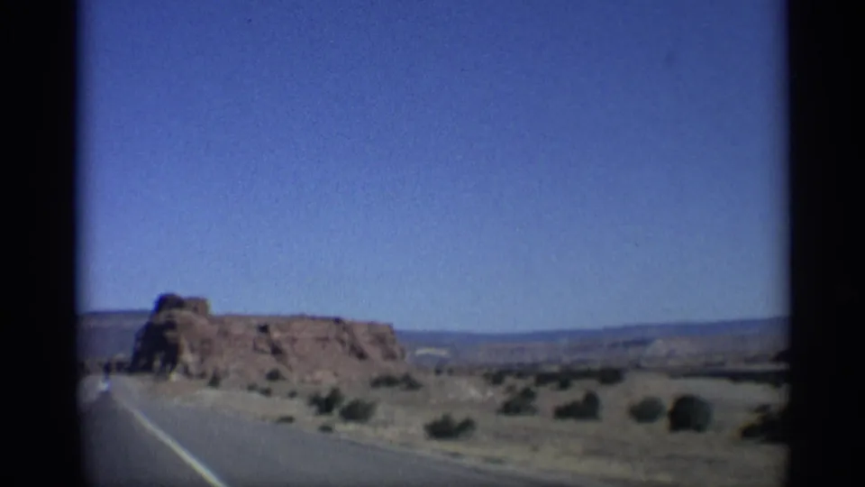 1959 Arizona home-movie view of a paved road approaching red rock formations with scrubland and distant horizon visible.