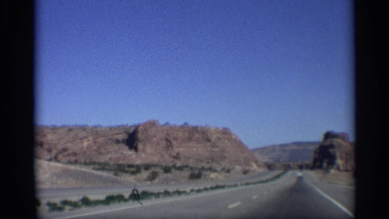 Desert highway running between red rock cuts under a clear blue sky.