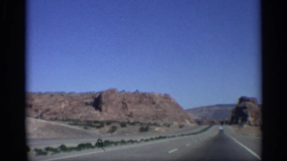 1959 Arizona 8mm road view from a moving vehicle, with a paved highway passing through red rock desert terrain.