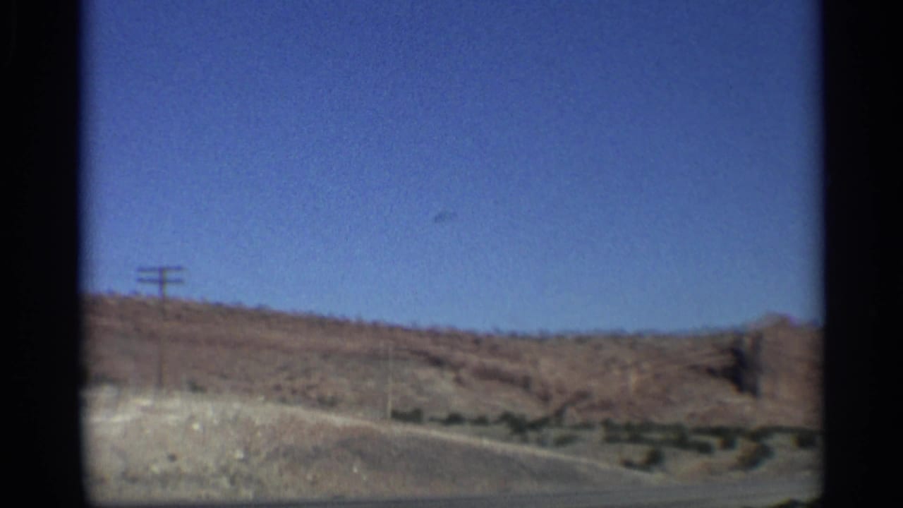 Roadside desert slope with utility poles and red rock terrain.