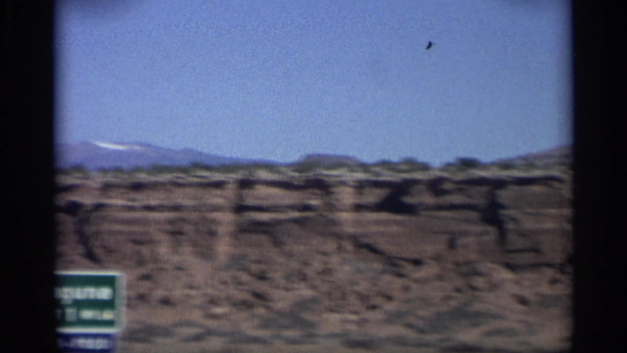 1959 Arizona 8mm frame showing a green Laguna roadside sign and layered desert plateaus beneath a clear sky.