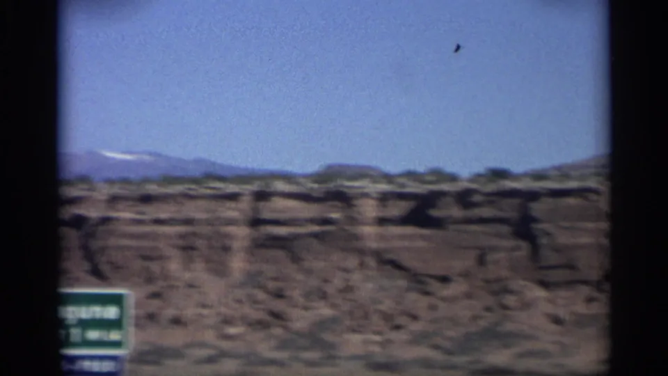 1959 Arizona 8mm frame showing a green Laguna roadside sign and layered desert plateaus beneath a clear sky.