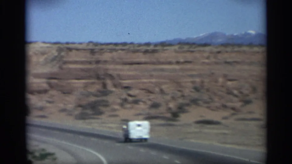 1959 Arizona road scene with a white camper-style vehicle traveling along a paved highway through red rock terrain.