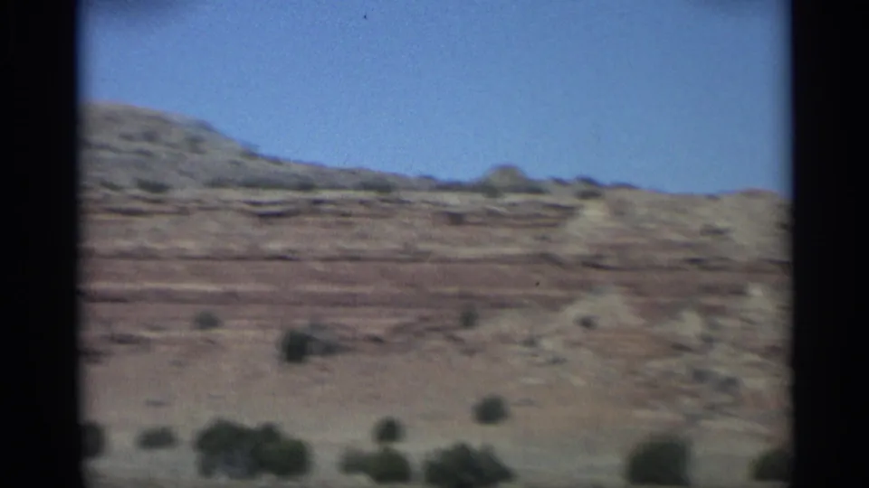 1959 Arizona landscape frame showing layered red rock plateaus, scrub vegetation, and low desert hills.
