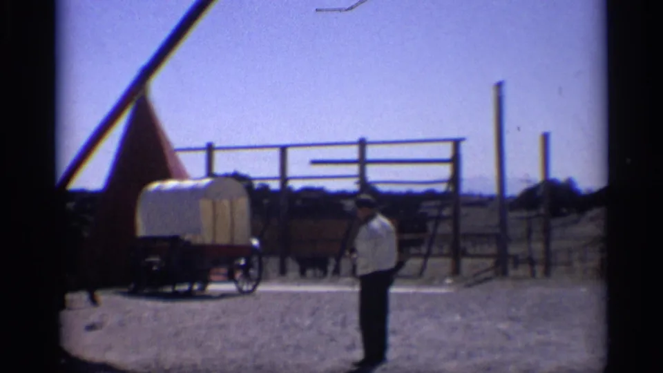 A man stands at the right side of the frame while the covered wagon, fencing, and western display remain visible in the Arizona sunlight.
