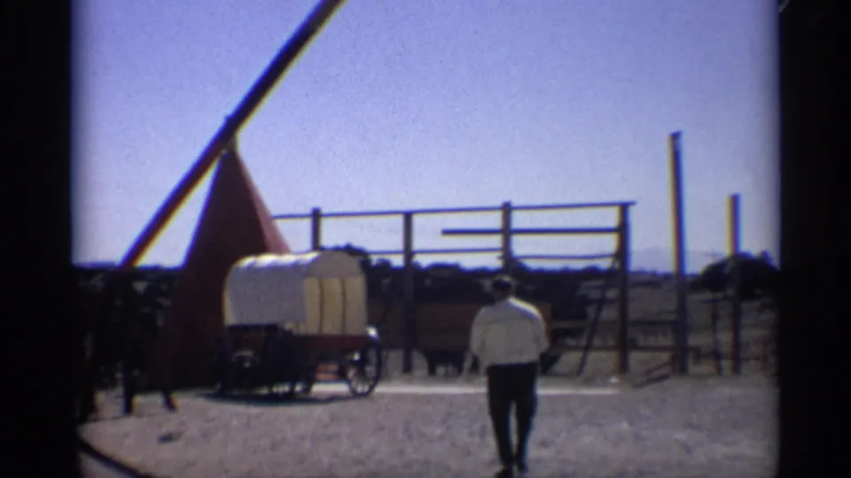 1959 Arizona home-movie view of a man walking toward a covered wagon, red teepee-style tent, fencing, and animals.