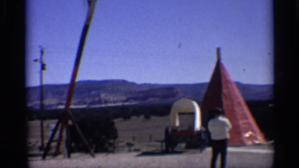 Wide 1959 Arizona frame with an adult man, covered wagon, red teepee-style tent, ranch yard, and distant hills.